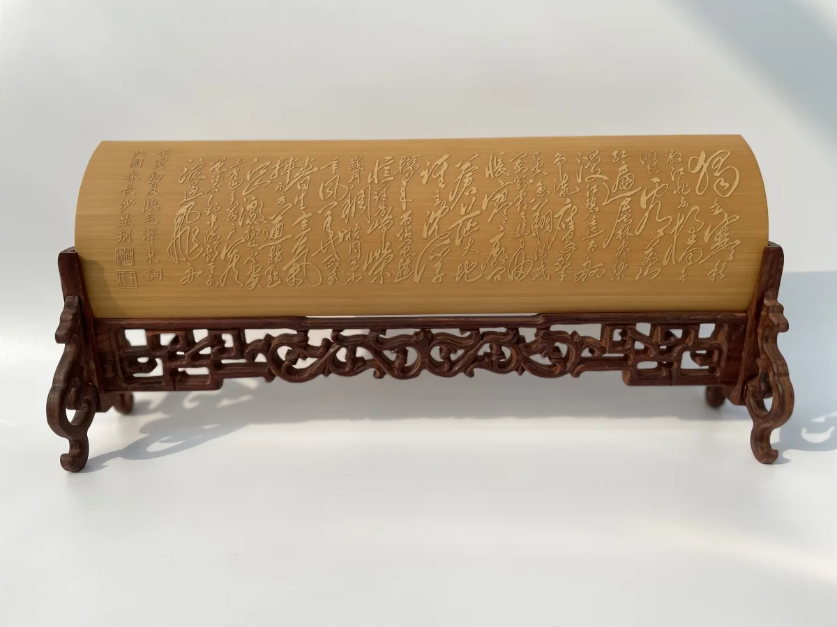 A bamboo wrist rest carved with a poem in flowing cursive script, on a carved hardwood stand