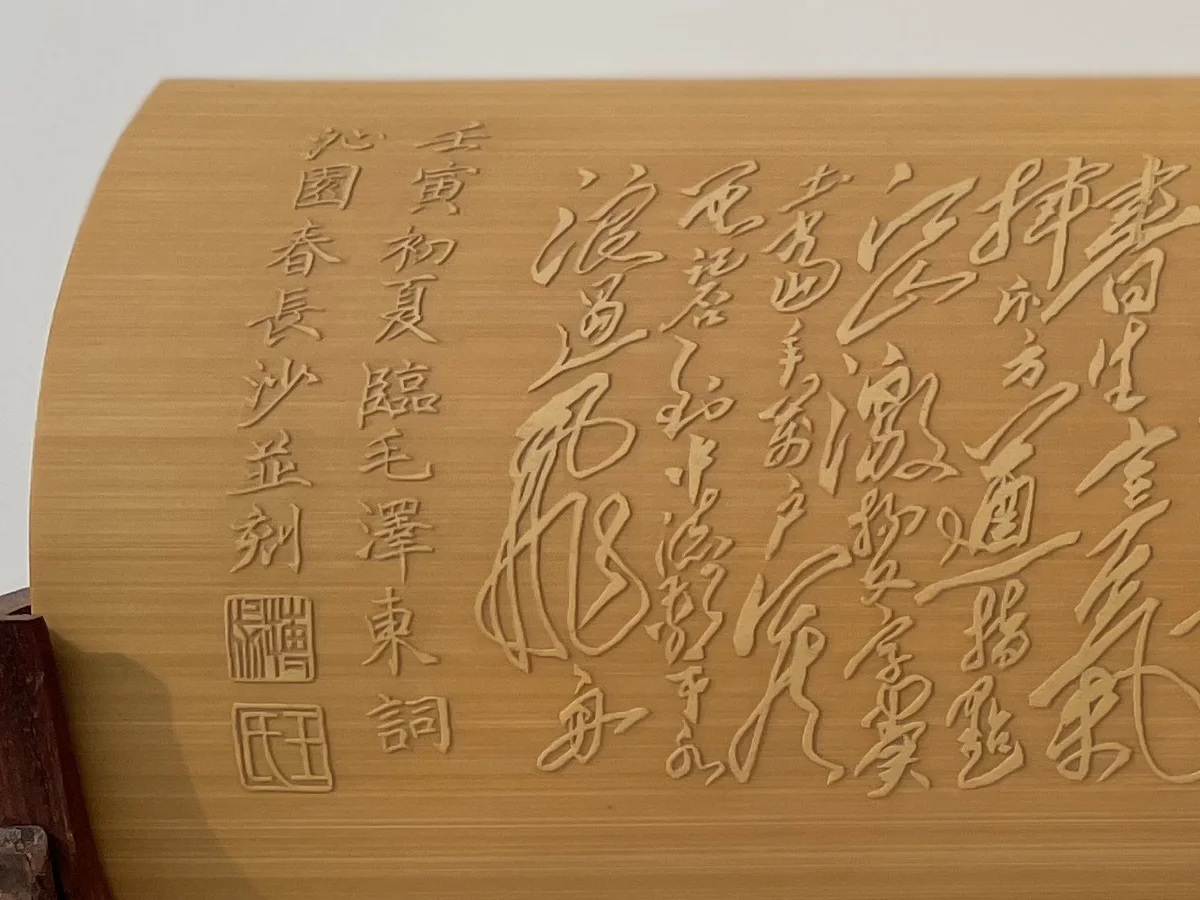 Close-up of a bamboo wrist rest: a vertical inscription in regular script and two small square seals carved into the bamboo