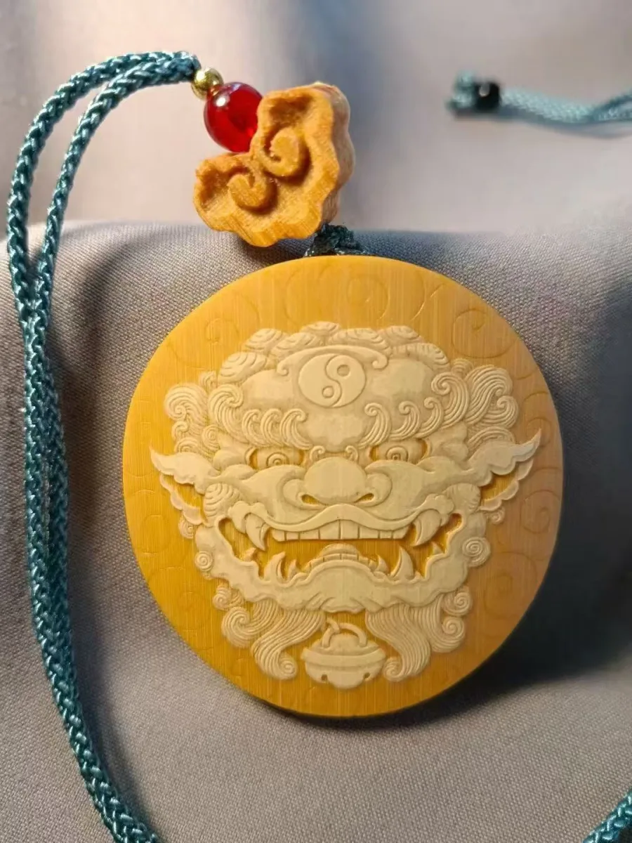 A round bamboo pendant carved with a guardian lion's face, hung on a teal cord with a red bead